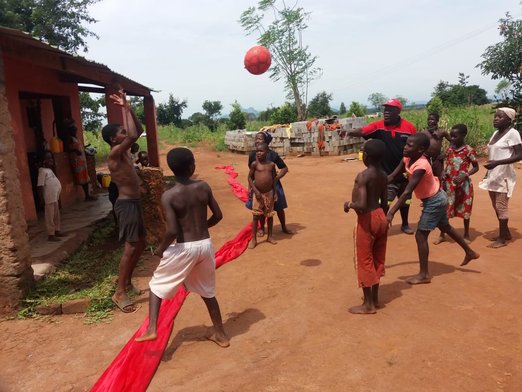 Barn och vuxna leker med en boll på röd torr jord