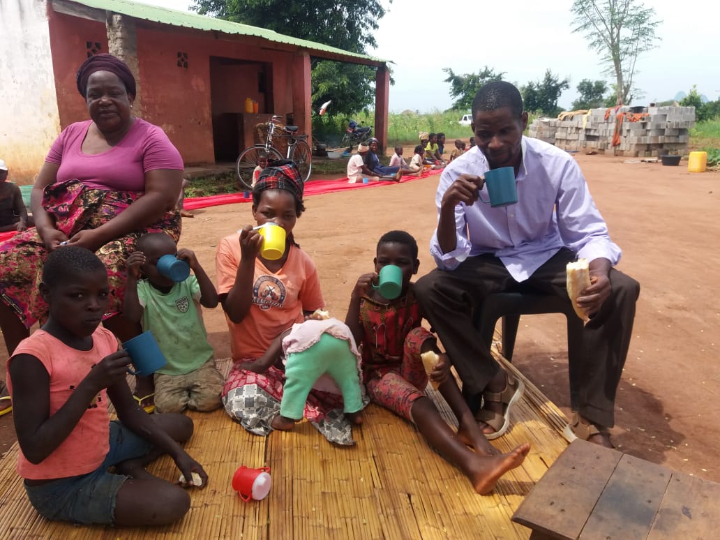 Två vuxna och fyra barn sitter och dricker och äter mat utanför sitt hus iMocambique