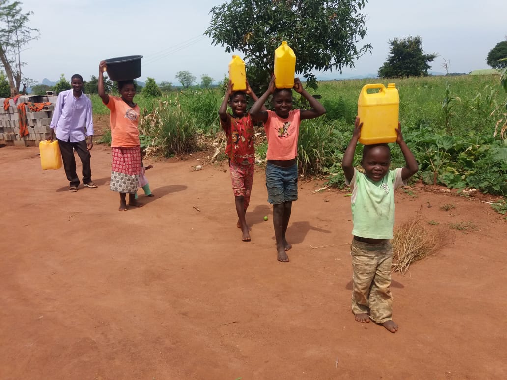 Barn och vuxna bär vattentankar på huvudet