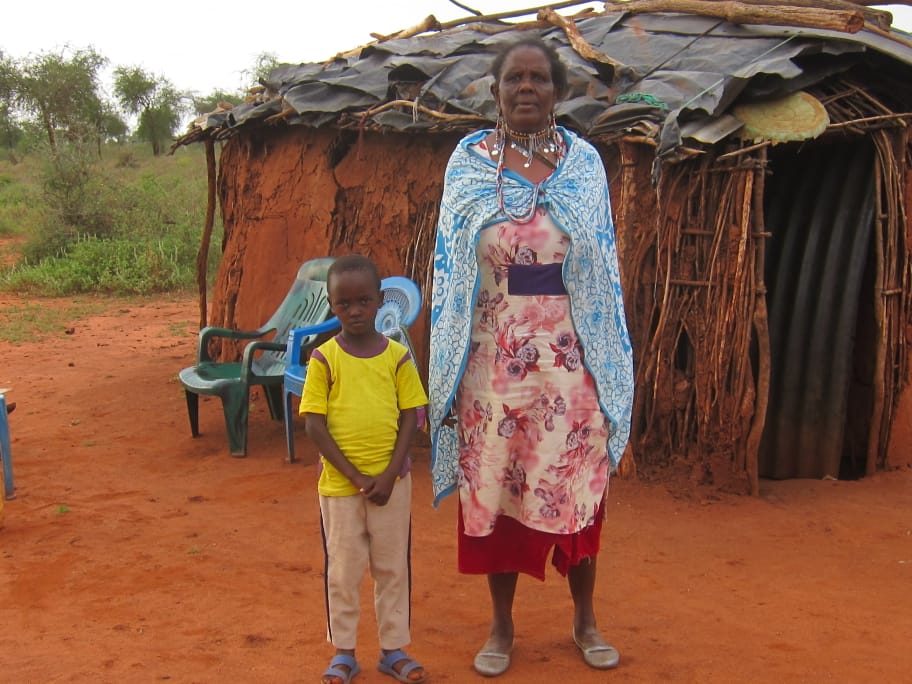 En pojke i Kenya och hans extramamma står framför en hydda.